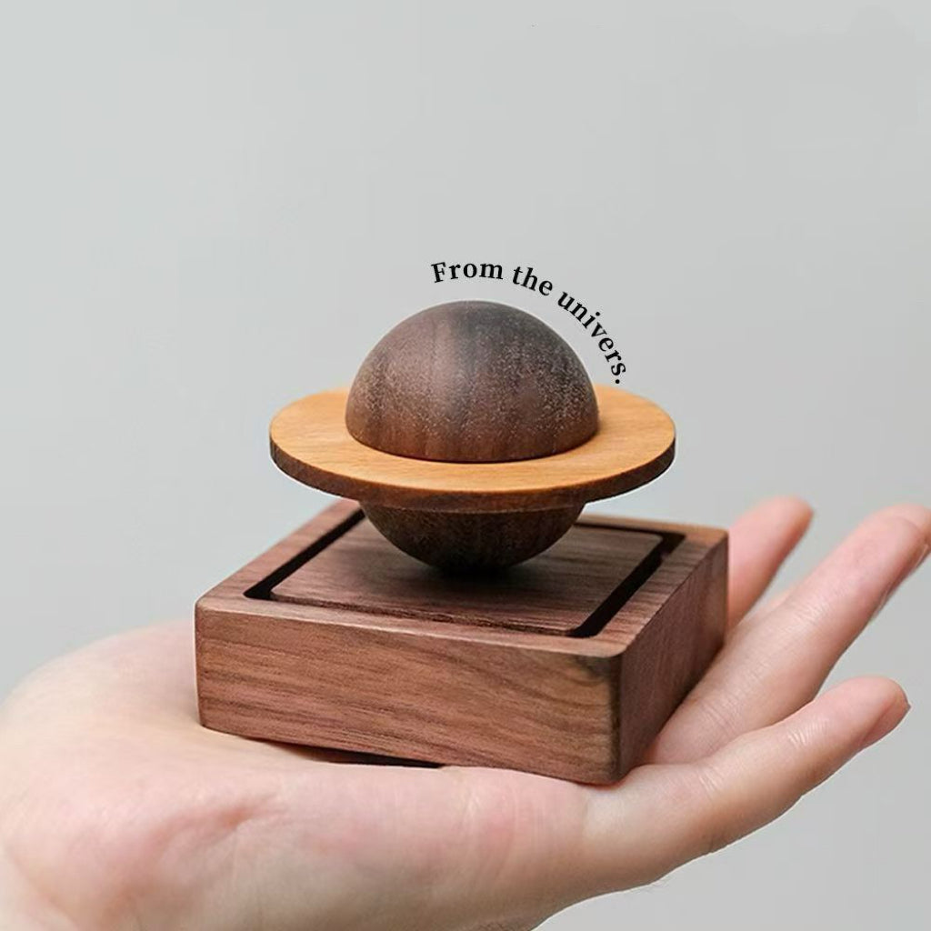 Saturn-shaped black walnut wooden aroma diffuser held in hands, minimalist mindfulness decor