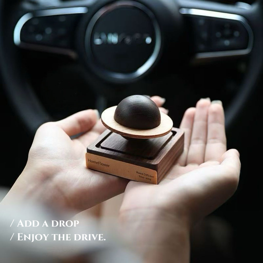 Wooden reed diffuser with a dark sphere on top held in hands
