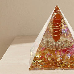 Close-up of a wealth motivation success orgonite energy pyramid with orange crystal point, copper coil and shimmering gold details