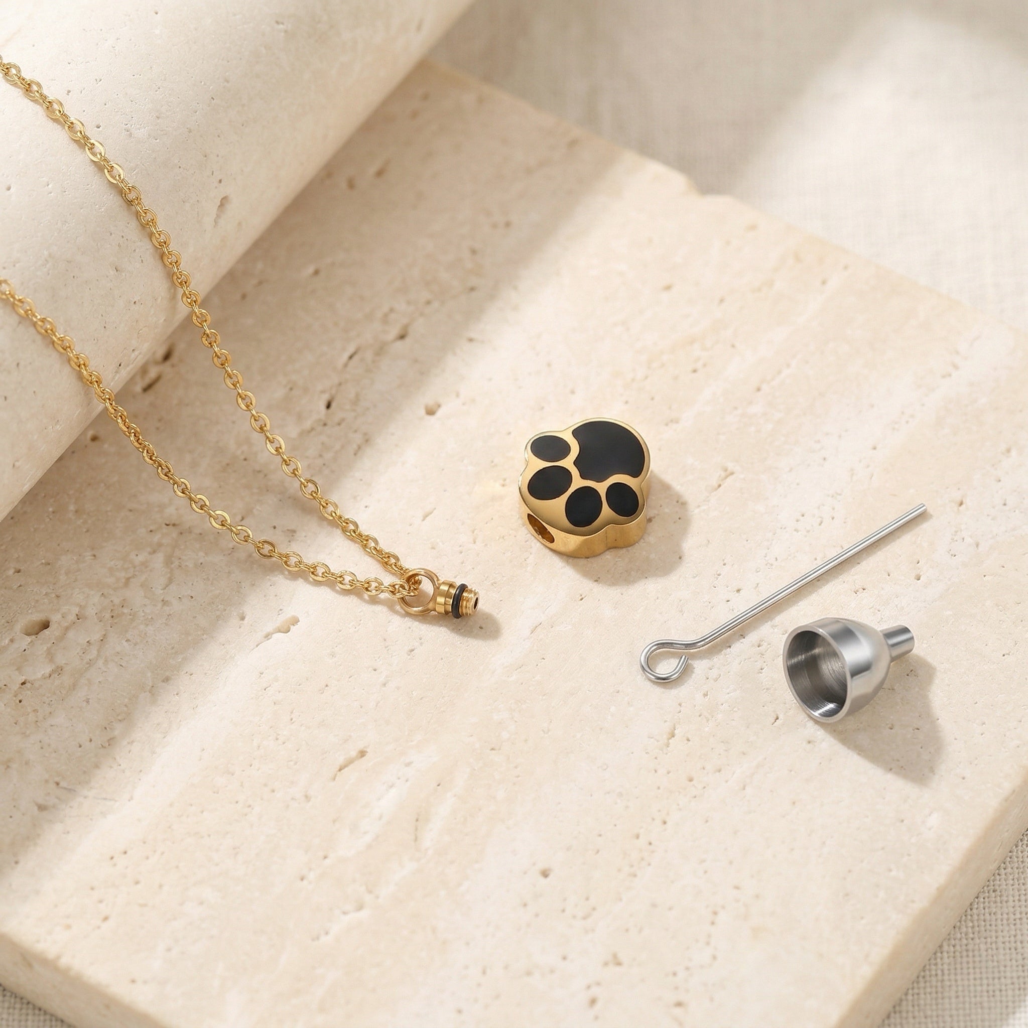 Gold necklace with a black and gold paw print charm on a beige surface.
