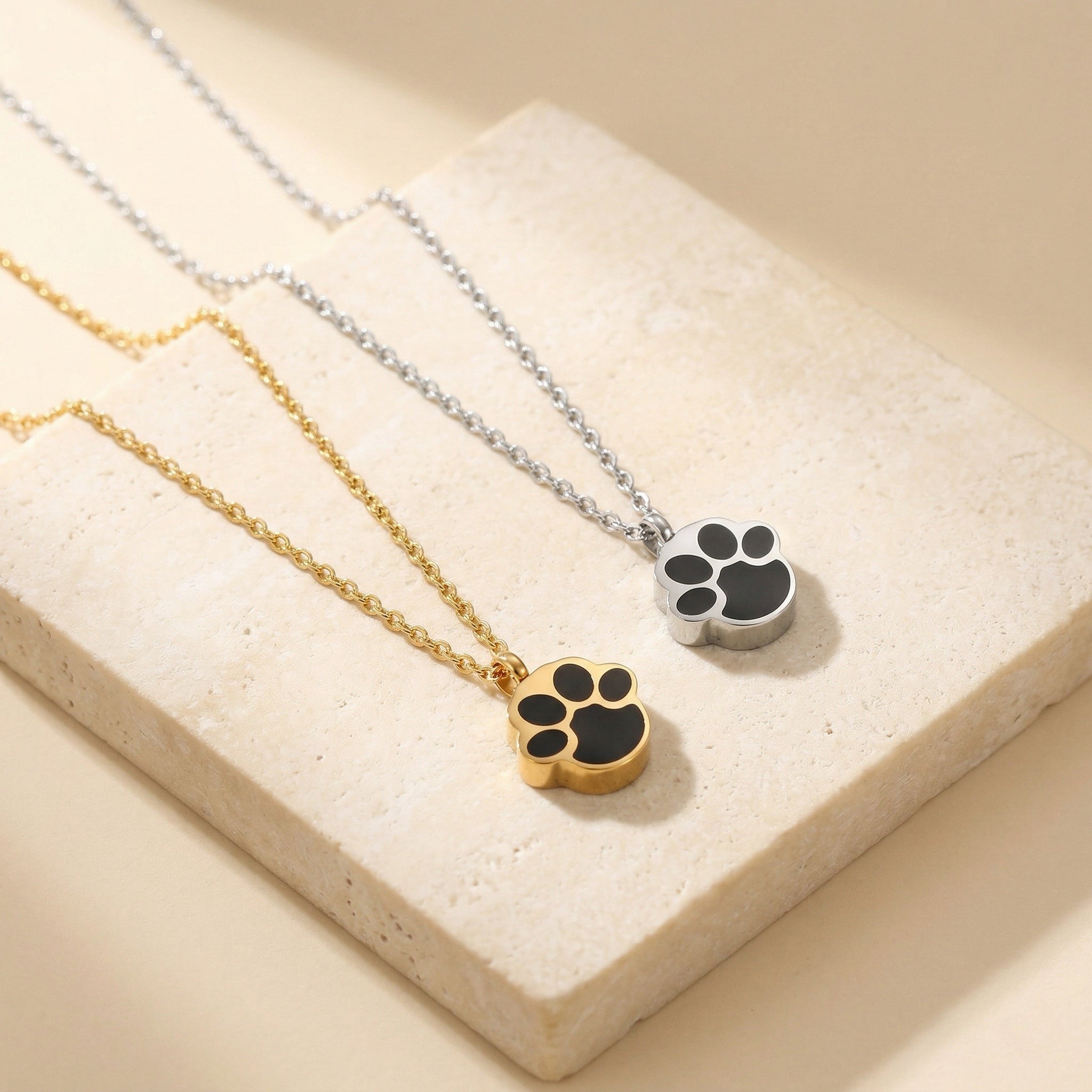 gold and silver paw print memorial necklaces on beige stone background