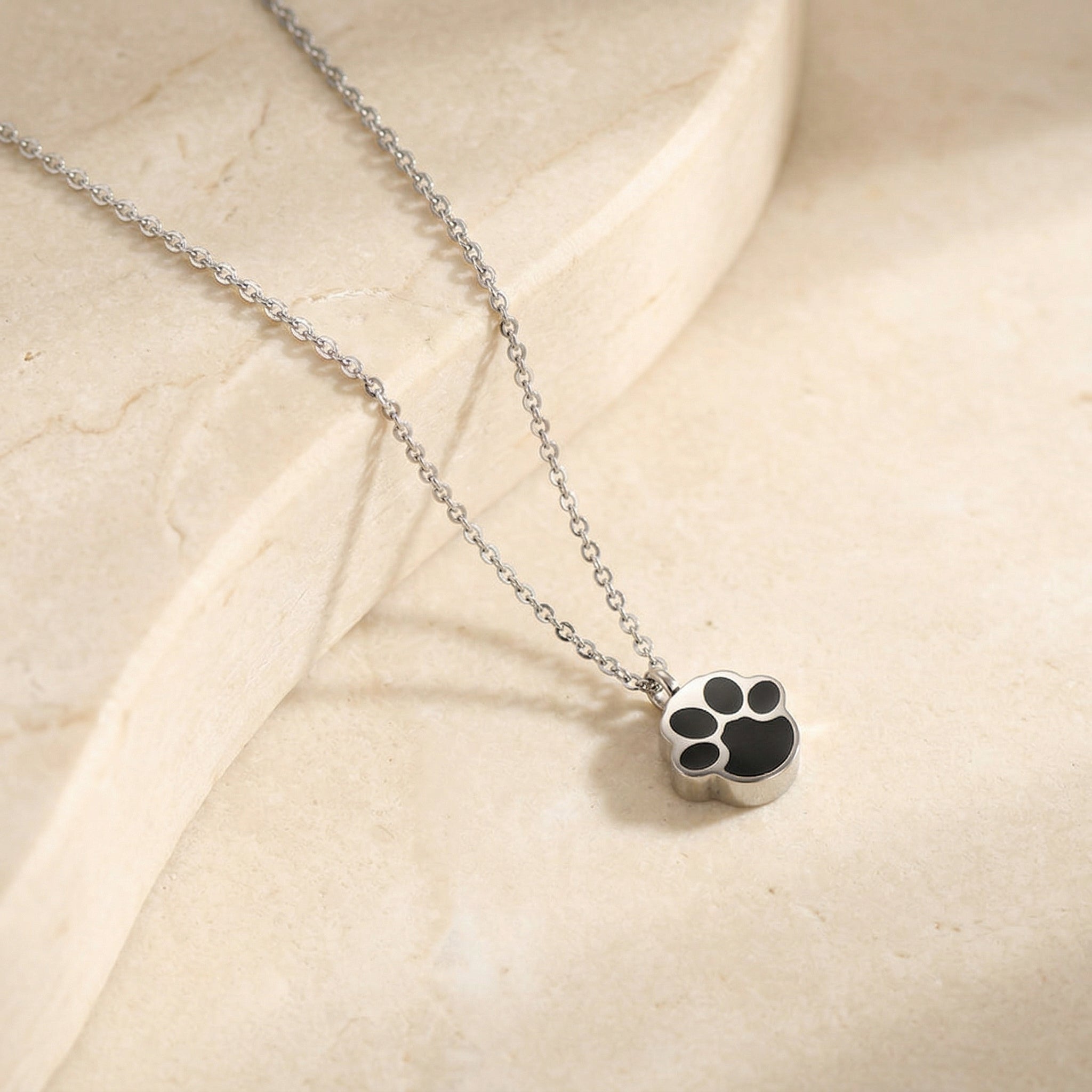 silver paw print memorial necklace on beige stone background