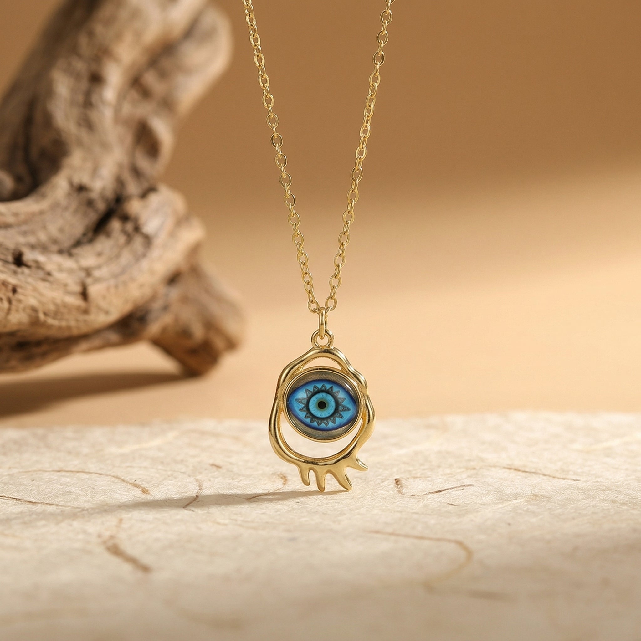 gold evil eye pendant necklace with blue starburst eye design on neutral background