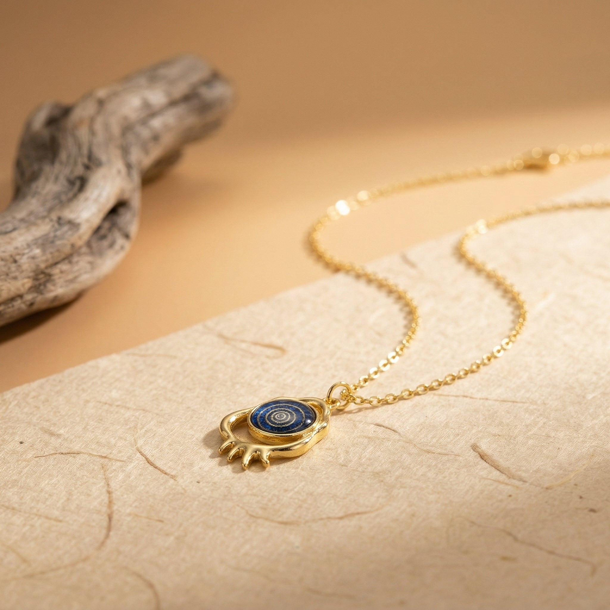 gold evil eye pendant necklace with deep blue circular eye detail on neutral surface