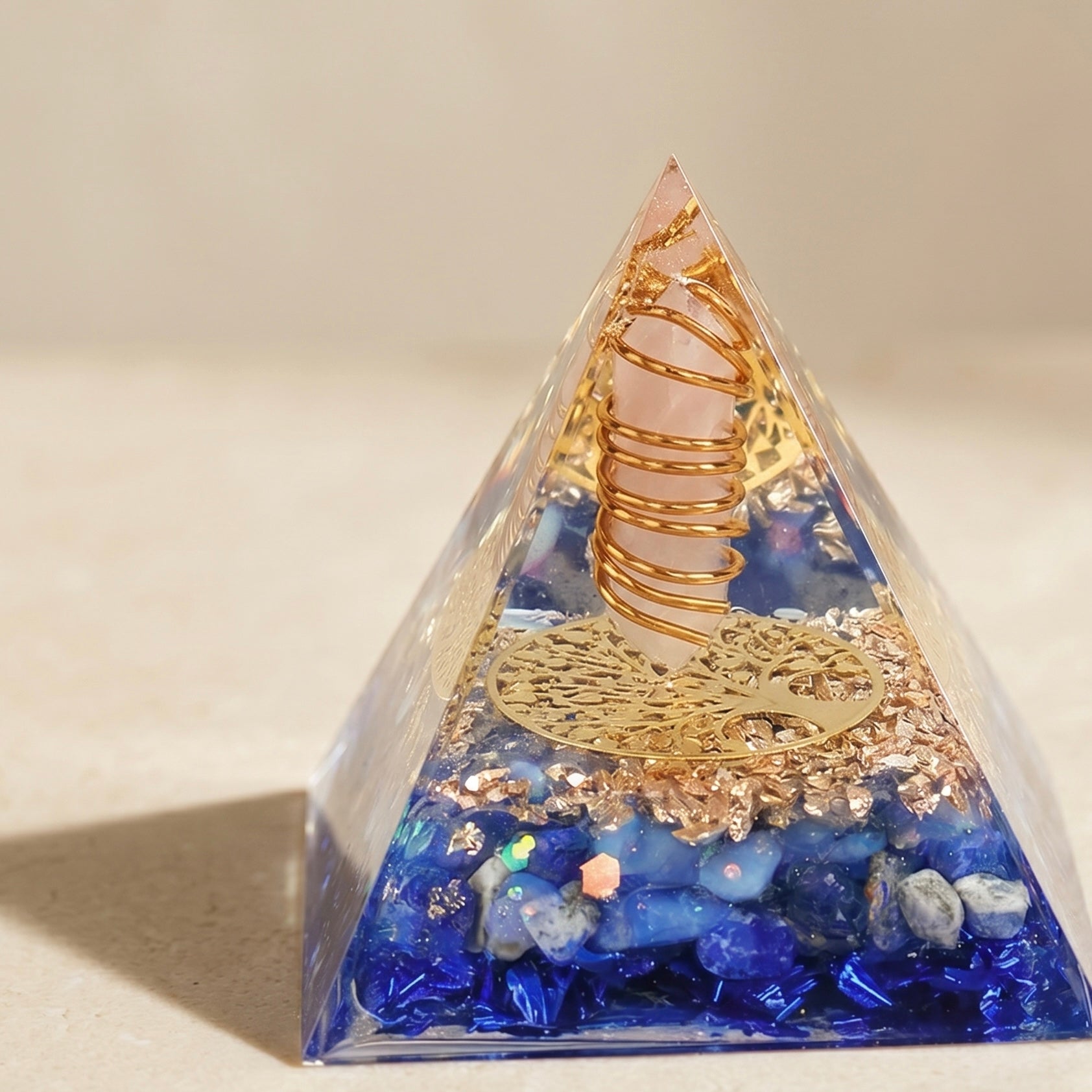 Emotional healing and inner peace orgonite pyramid with rose quartz point, lapis lazuli chips and copper coil on a neutral background