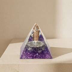 Intuition and inner guidance orgonite pyramid with amethyst chips, clear quartz point, copper coil and silver totem on a neutral background