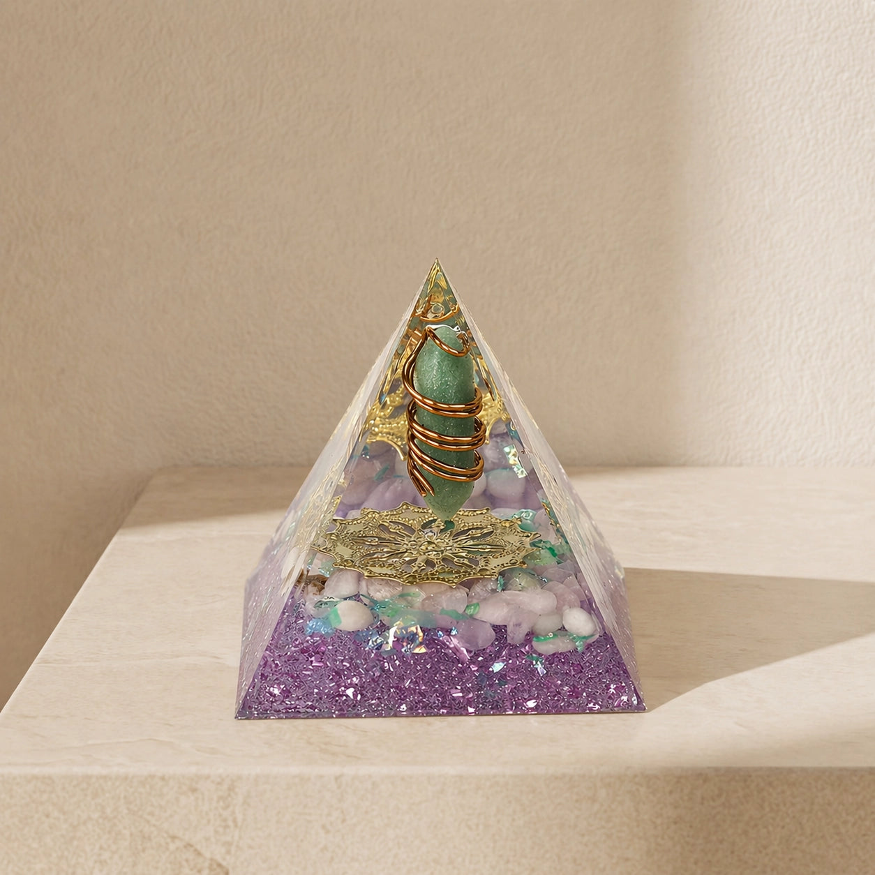 orgonite pyramid with green aventurine point, rose quartz chips, copper coil and gold totem on a neutral background
