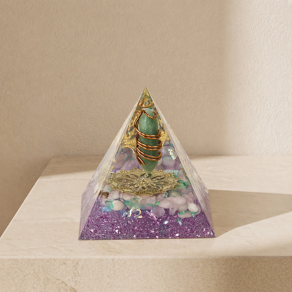 orgonite pyramid with green aventurine point, rose quartz chips, copper coil and gold totem on a neutral background