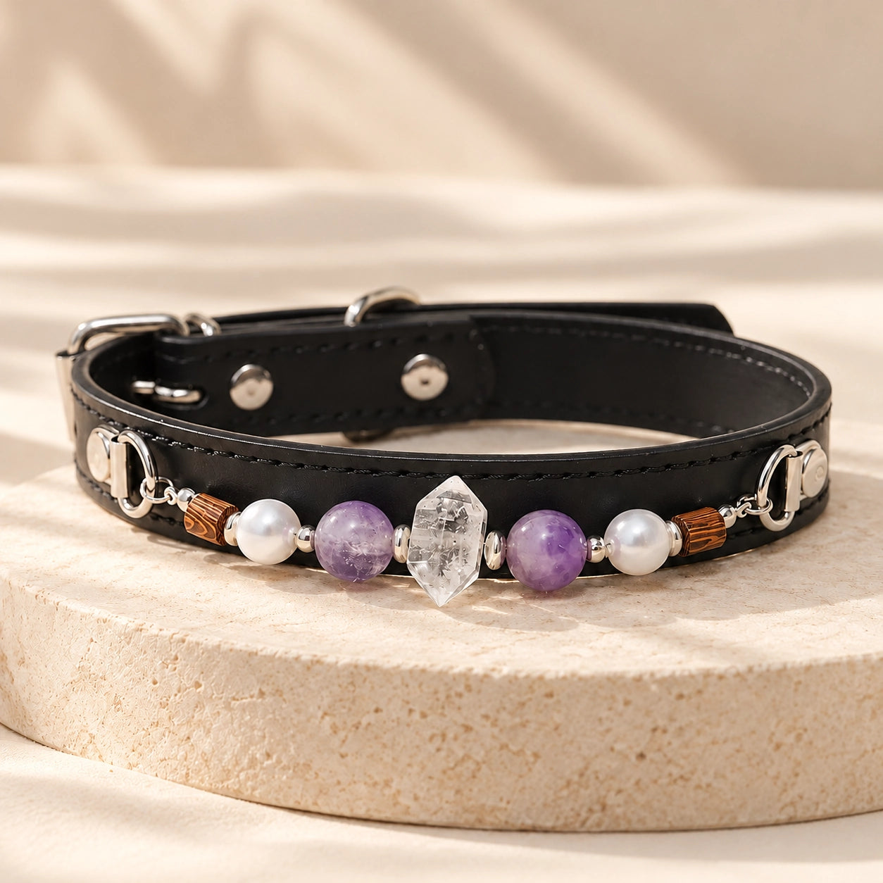 Black adjustable PU leather dog collar with purple amethyst beads and natural clear quartz centerpiece on a cream stone stand