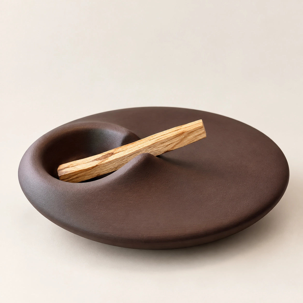 Sculptural earthy brown concrete Palo Santo holder with a natural wood stick on a warm greige background