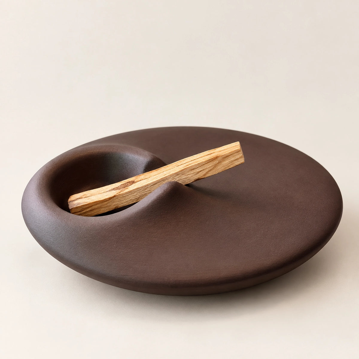 Sculptural earthy brown concrete Palo Santo holder with a natural wood stick on a warm greige background