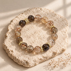 Overhead view of a smoky quartz and black gold rutilated quartz bracelet with polished beads and gold-tone spacers
