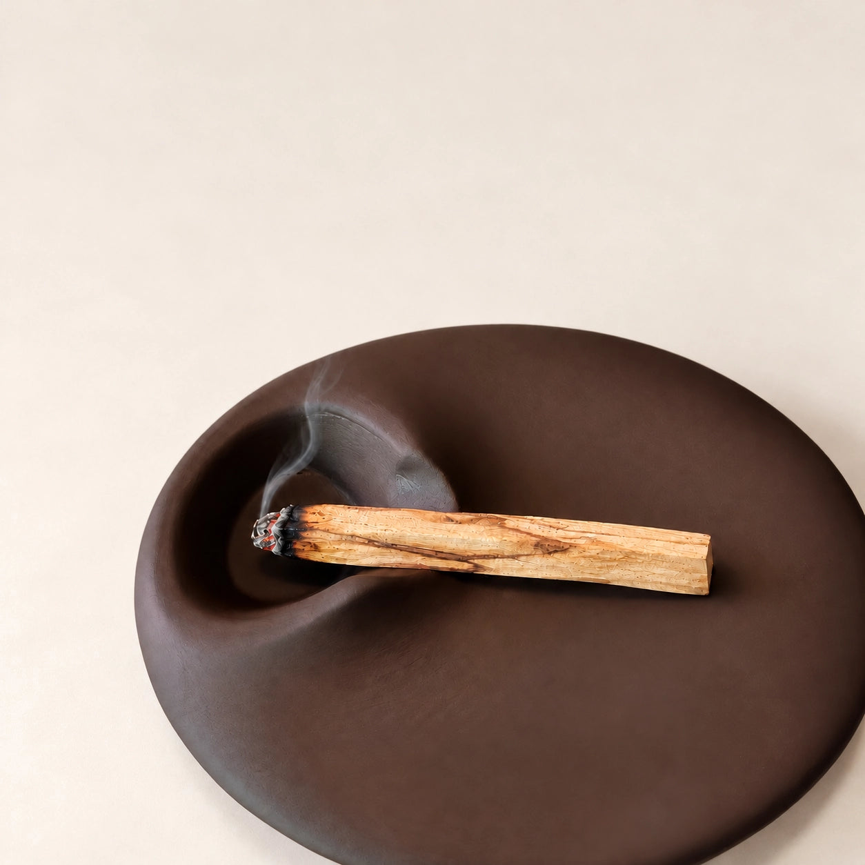Palo Santo stick with a smoldering tip over the recessed side of a sculptural brown concrete holder