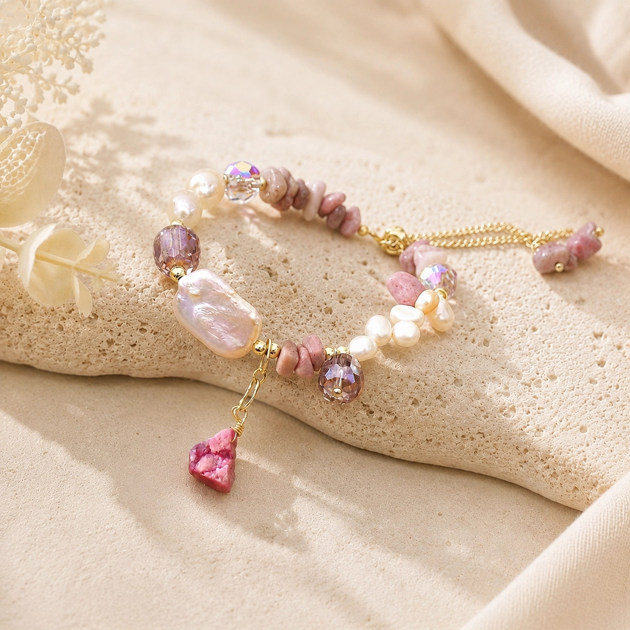 Rhodonite and baroque freshwater pearl bracelet draped across a cream stone pedestal