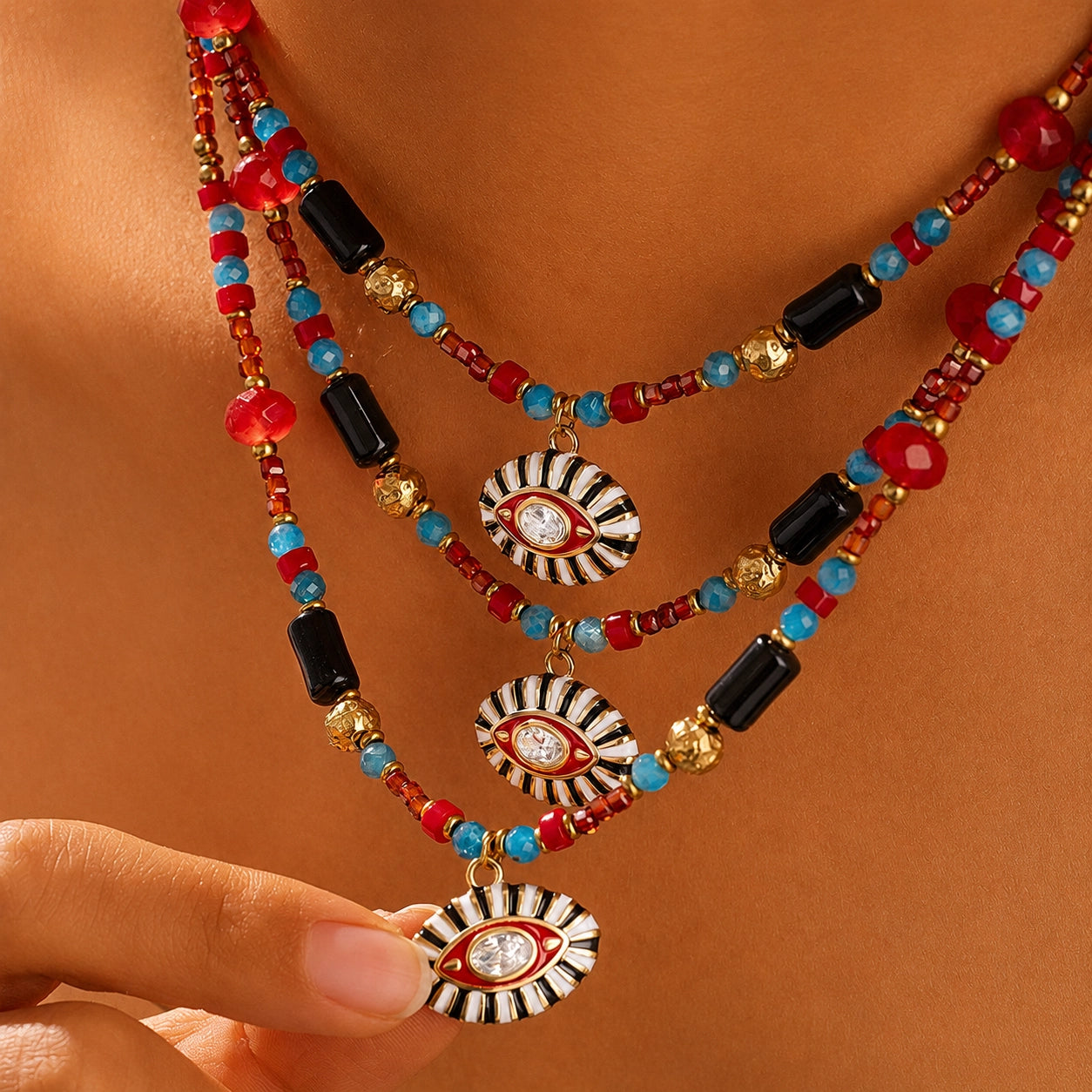 Close-up of model wearing three layered Evil Eye gemstone necklaces and holding the enamel pendant