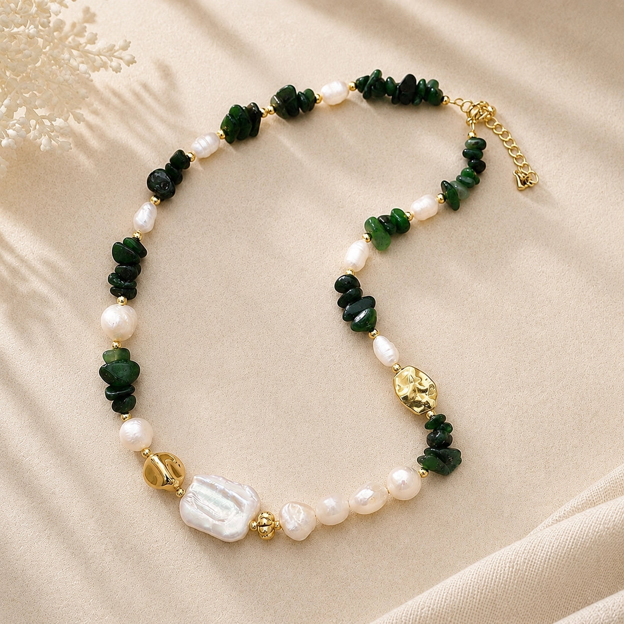 Green jade and freshwater pearl necklace with gold-plated accents arranged on cream fabric