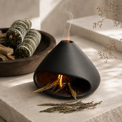 Black chimney-style sage burner with cleansing herbs and smoke in a sunlit ritual space