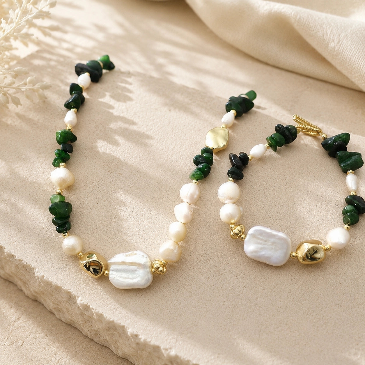 Green jade and freshwater pearl necklace and bracelet options styled together on a stone pedestal