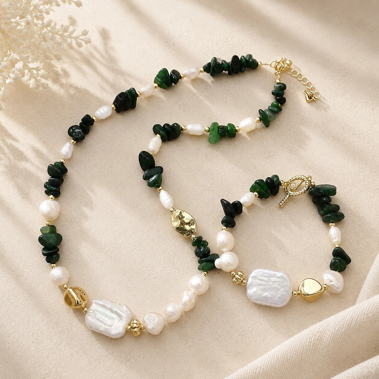 Green jade and freshwater pearl necklace and bracelet displayed together on soft cream fabric