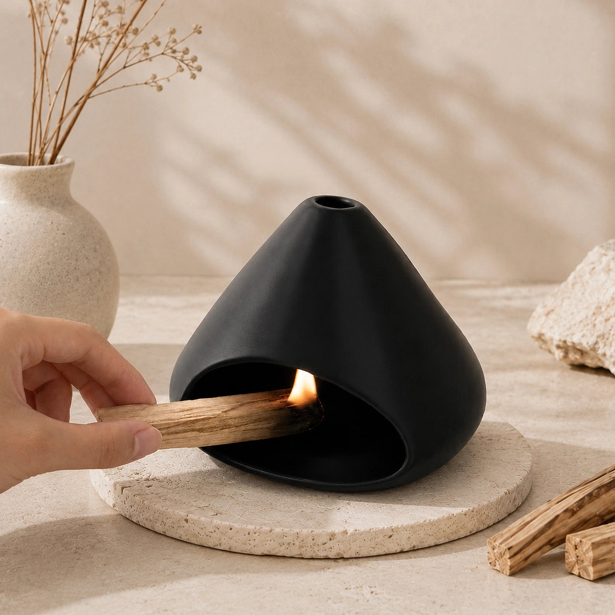 Hand lighting Palo Santo inside a matte black ceramic burner in a warm Wabi-Sabi setting