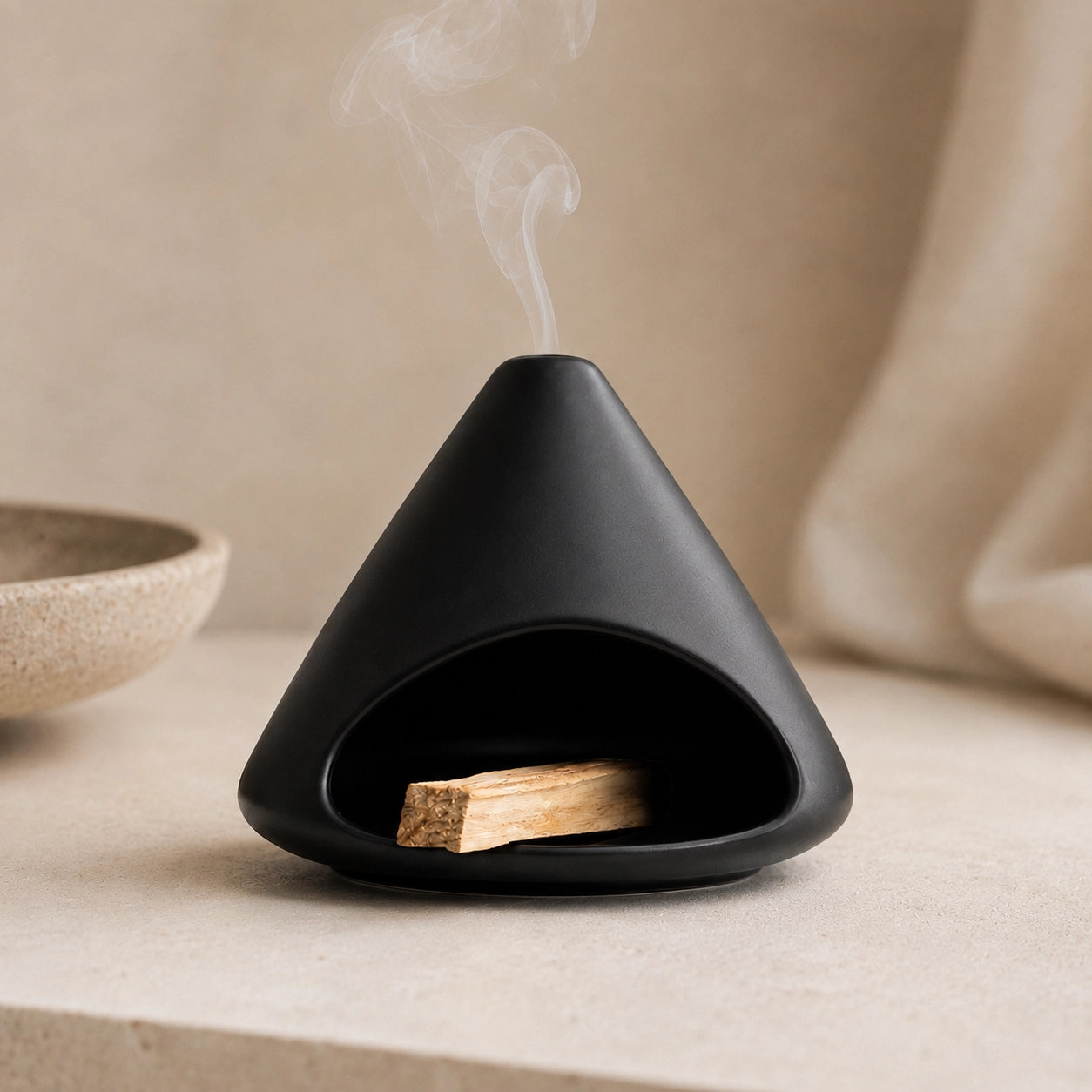 Matte black ceramic Palo Santo burner with wood inside and smoke rising through the chimney-style top vent
