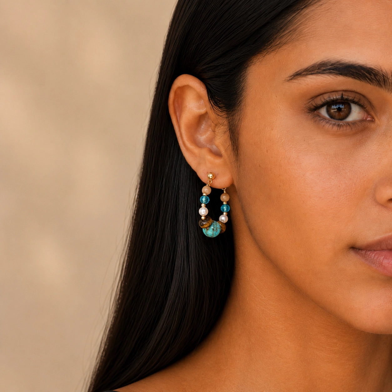 Close-up of a model wearing Tiger Eye and Turquoise earrings on a soft beige background