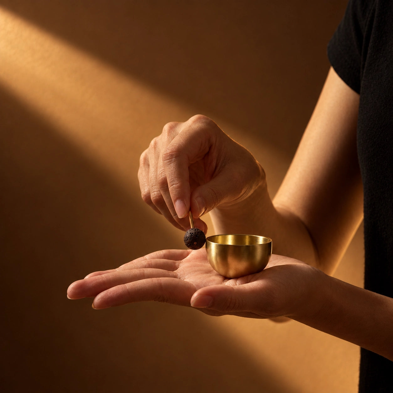 Mini aromatherapy singing bowl set with solid brass bowl and porous lava stone striker in warm natural light
