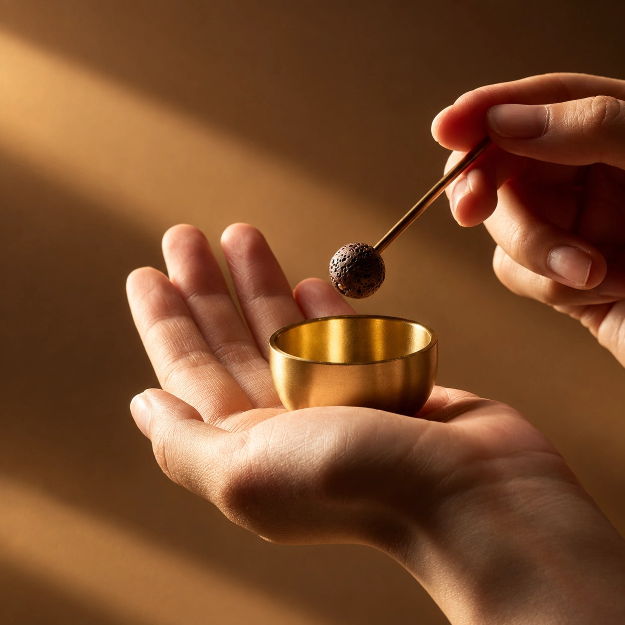 Palm-sized brass singing bowl held in one hand while a lava stone striker gently taps the rim