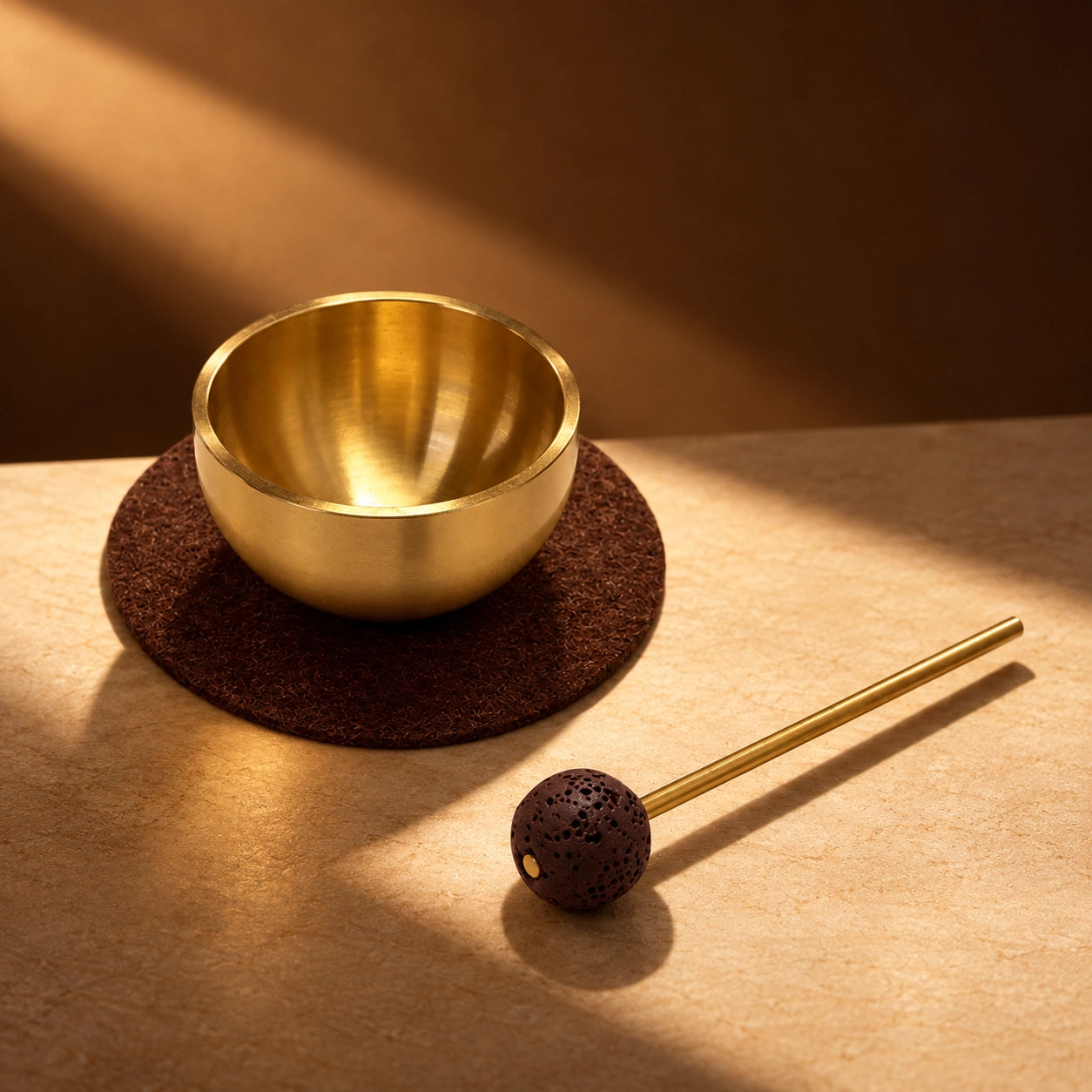 Mini brass singing bowl on a felt cushion with lava stone striker displayed beside it in warm light