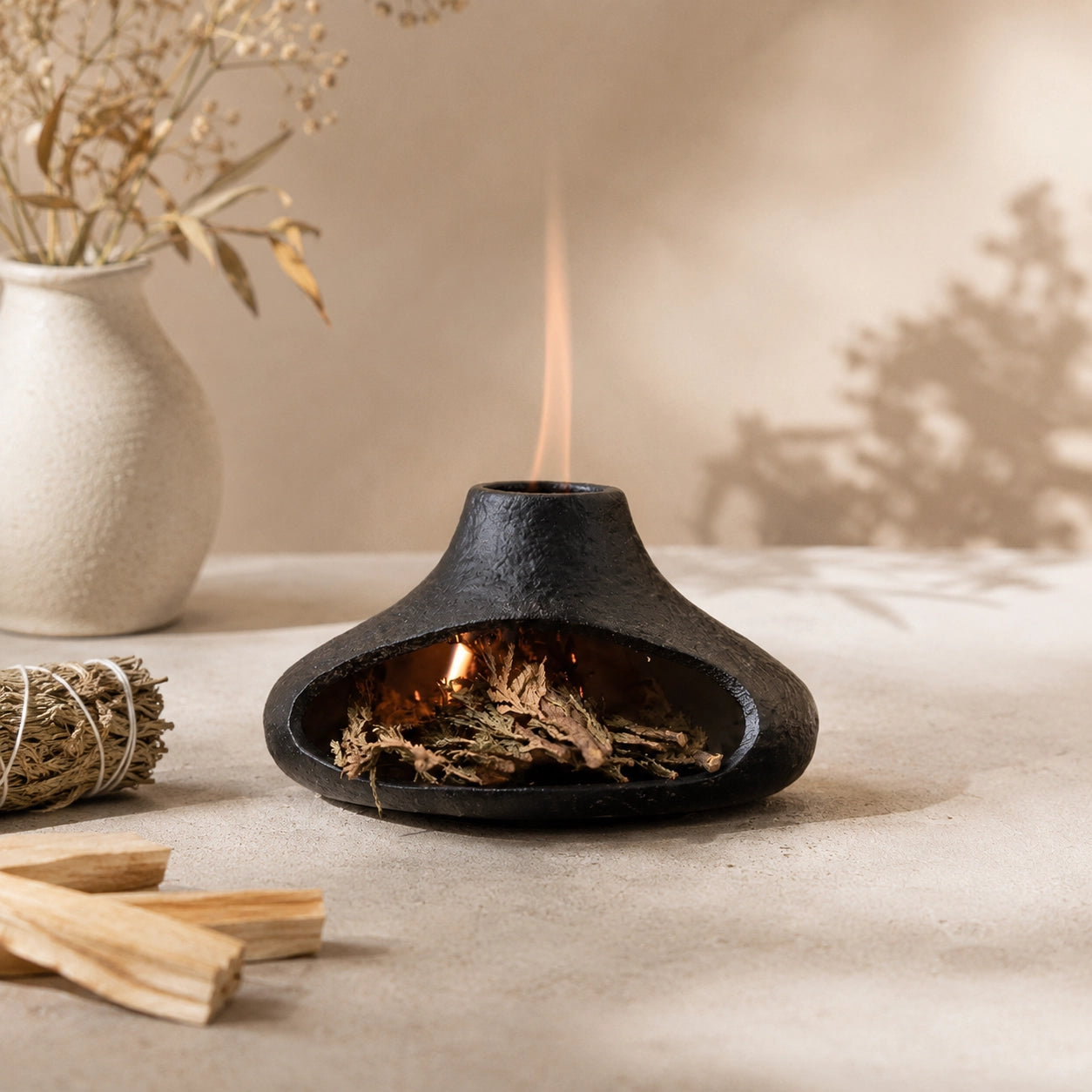 Black ceramic smudge bowl burning dried sage with smoke rising through the chimney opening