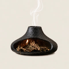 Black chimney-style ceramic Palo Santo burner with dried sage and smoke on a warm ivory background