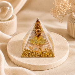 Abundance and wealth manifestation orgonite pyramid with tiger’s eye, citrine, copper coil, and gold foil on a warm neutral display stand