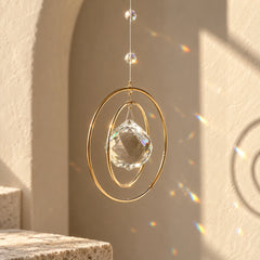 Golden Orbit crystal suncatcher with faceted clear quartz and golden rings reflecting rainbow light in a calm neutral interior