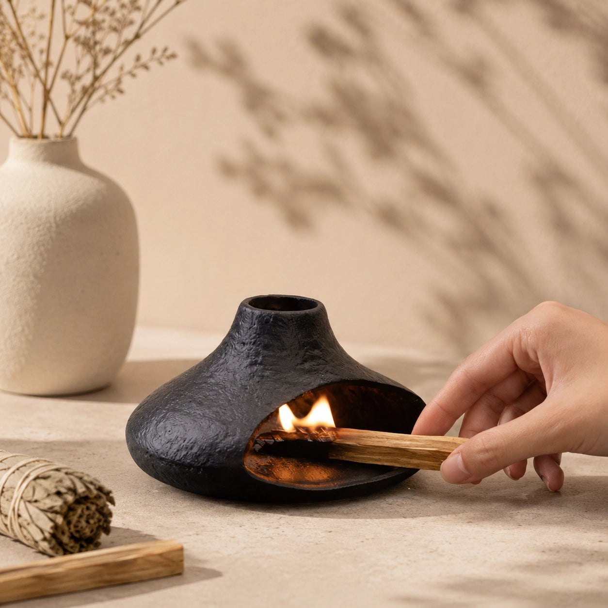 Hand placing a lit Palo Santo stick inside a black chimney-style ceramic burner