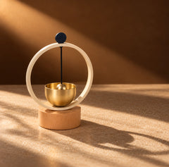Mini brass singing bowl chime with circular frame and wooden base in warm amber natural light