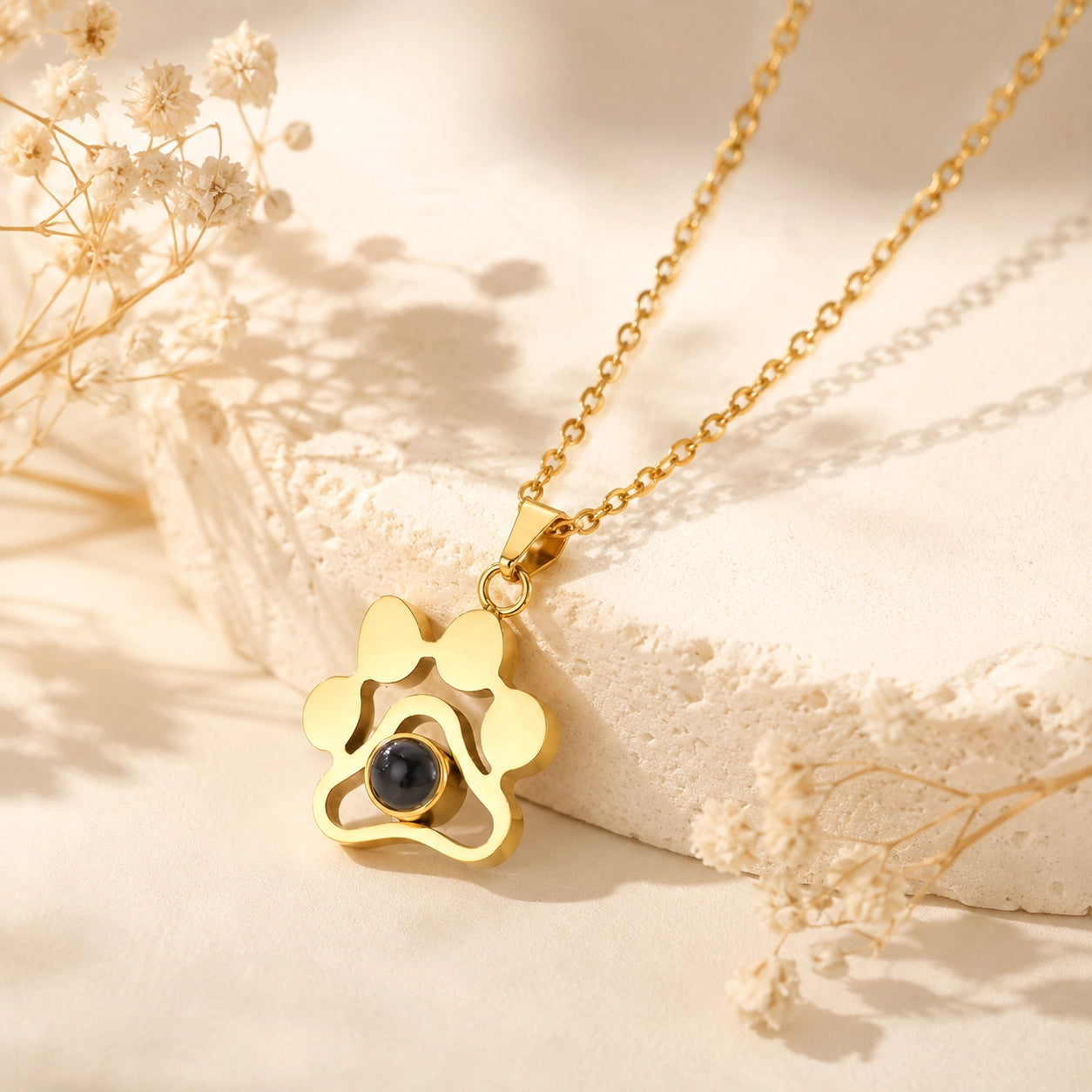 Gold personalized pet photo projection necklace with paw print pendant on a warm cream background