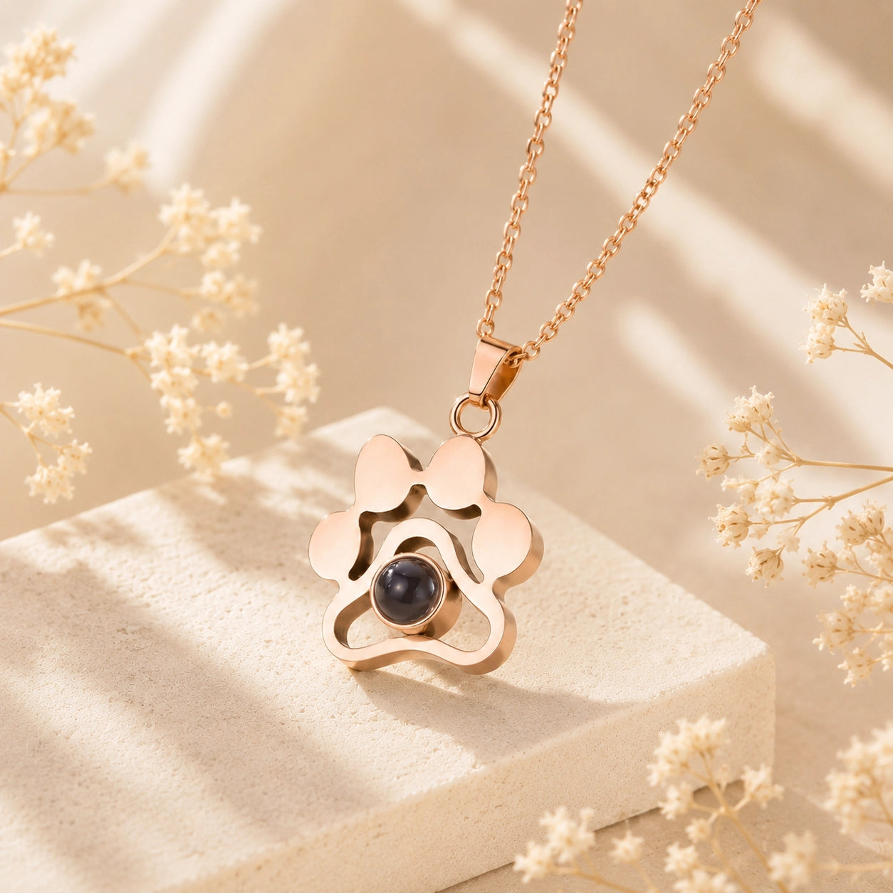 Rose gold personalized pet photo projection necklace with paw print pendant on a cream stone display