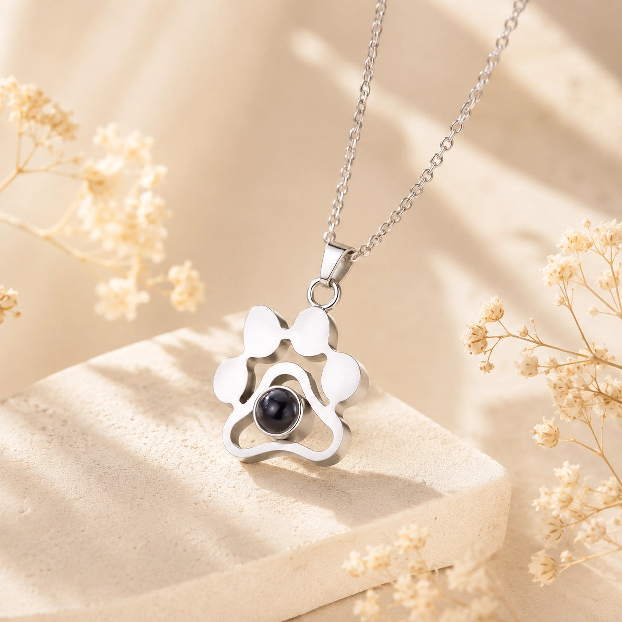 Silver personalized pet photo projection necklace with paw print pendant on a cream stone display