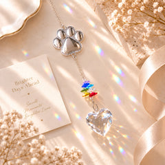 Heart-shaped pet paw crystal suncatcher with colorful star beads and rainbow reflections in a warm ivory flat lay
