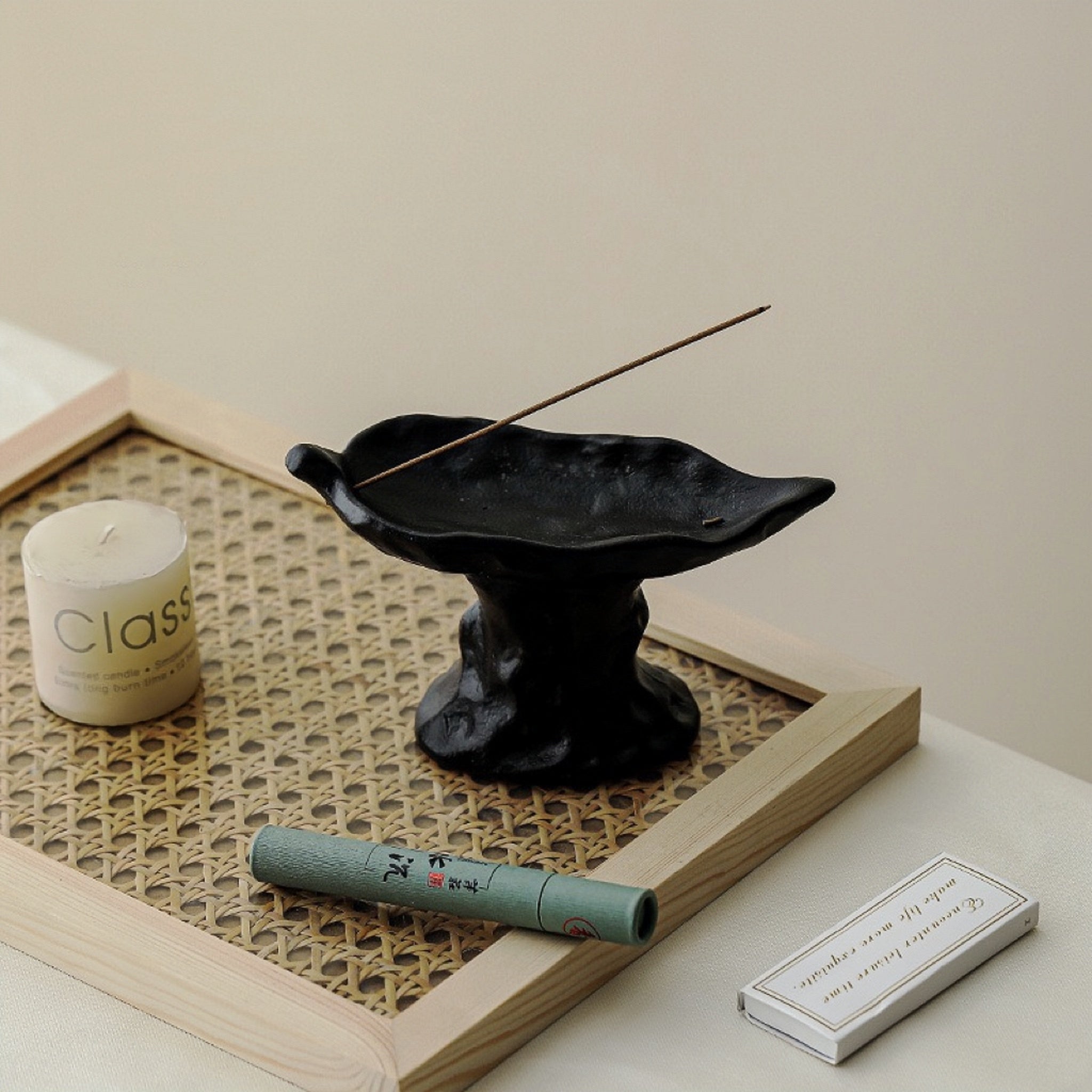 Incense burner with incense stick, candle, and packaging on a textured surface