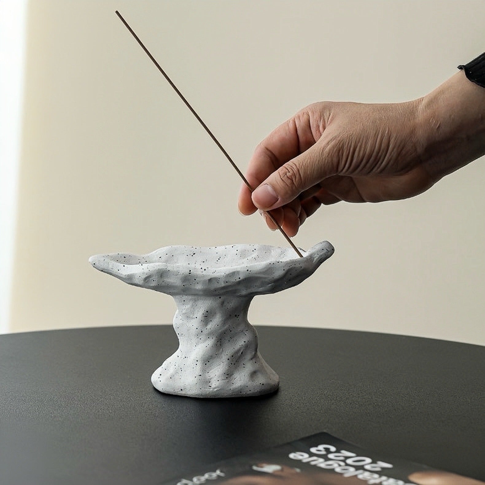 Person lighting an incense stick over a textured white ceramic incense holder on a dark surface.