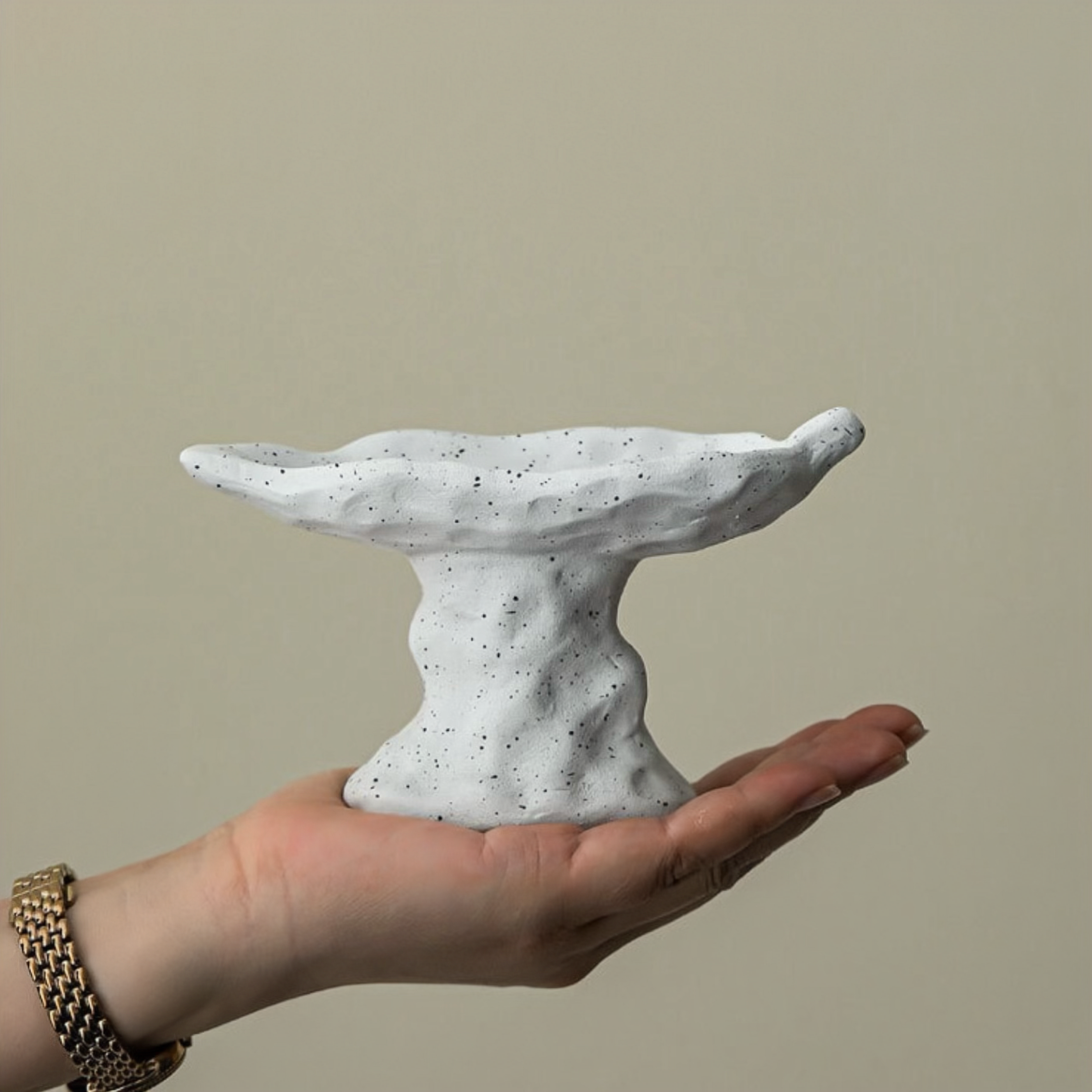 Hand holding a small, textured stone-like sculpture against a plain background