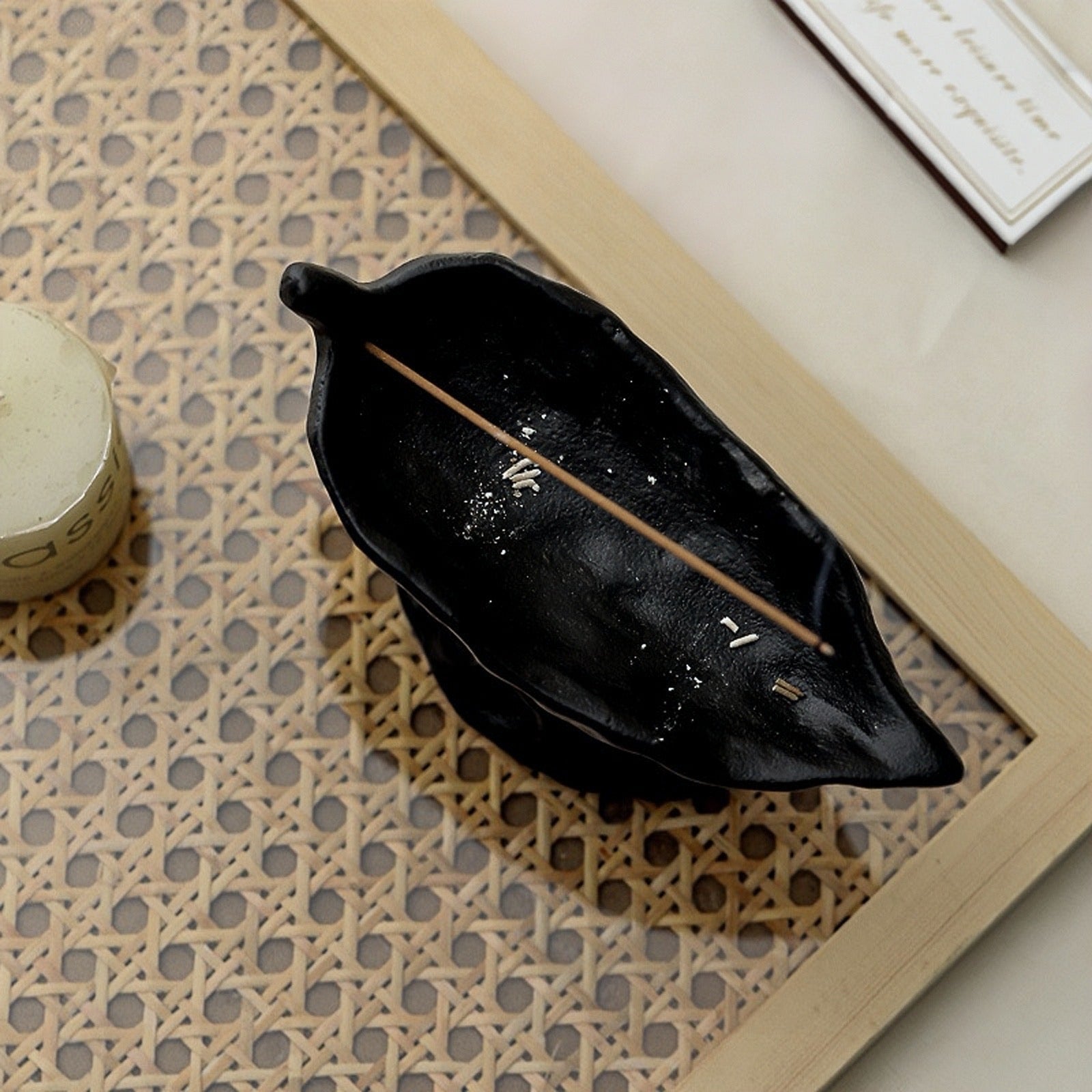 Black leaf-shaped container with a wooden stick on a textured surface
