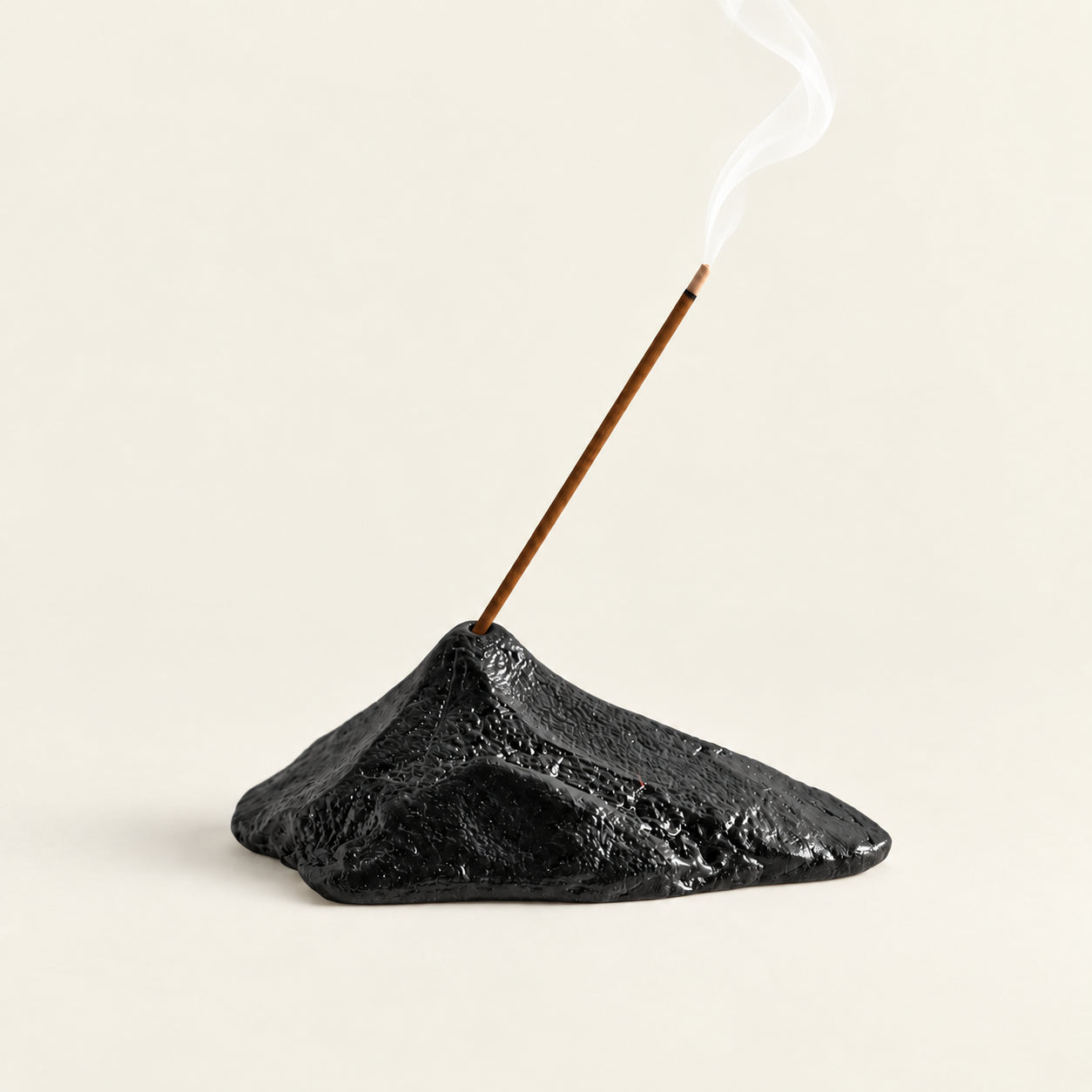 Black sculptural mountain ceramic incense stick holder with burning incense on a warm ivory background