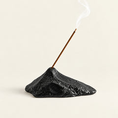 Black sculptural mountain ceramic incense stick holder with burning incense on a warm ivory background