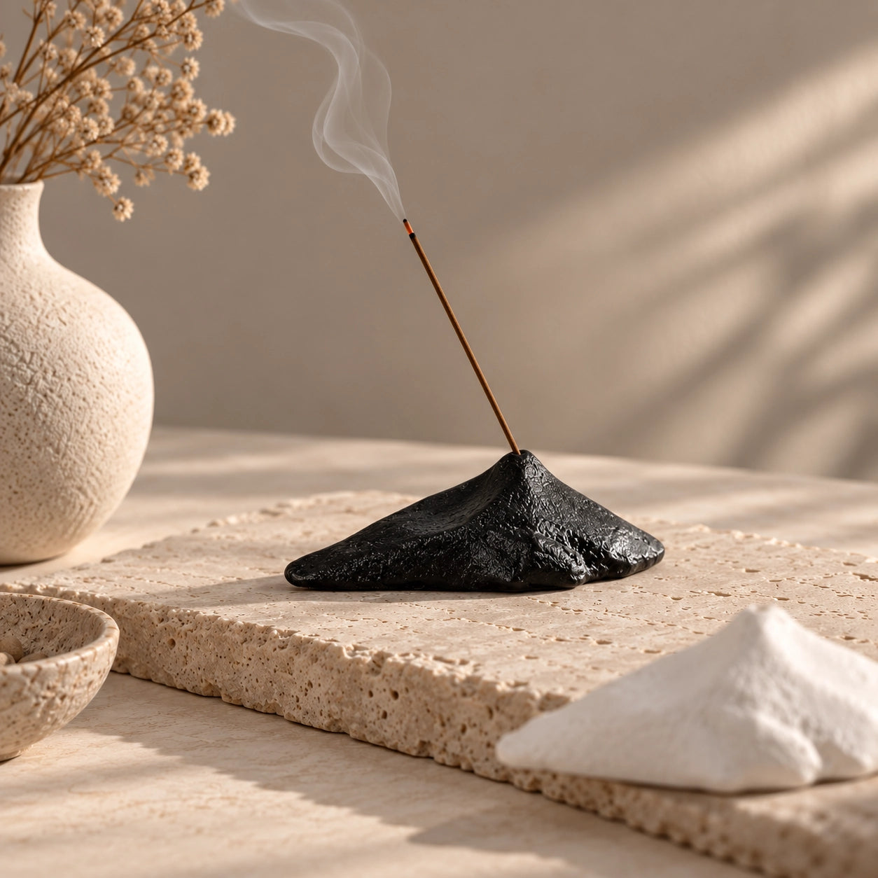 Black mountain-shaped ceramic incense stick holder with white option softly blurred in the foreground