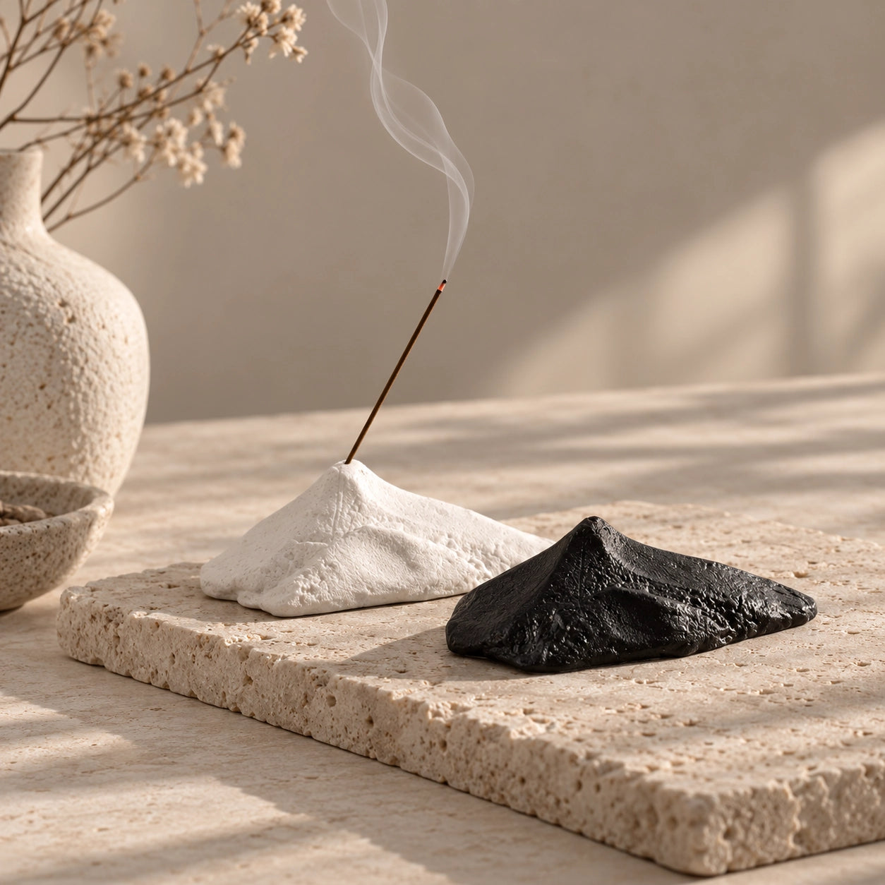 Black and white sculptural mountain ceramic incense stick holders styled together on a stone slab