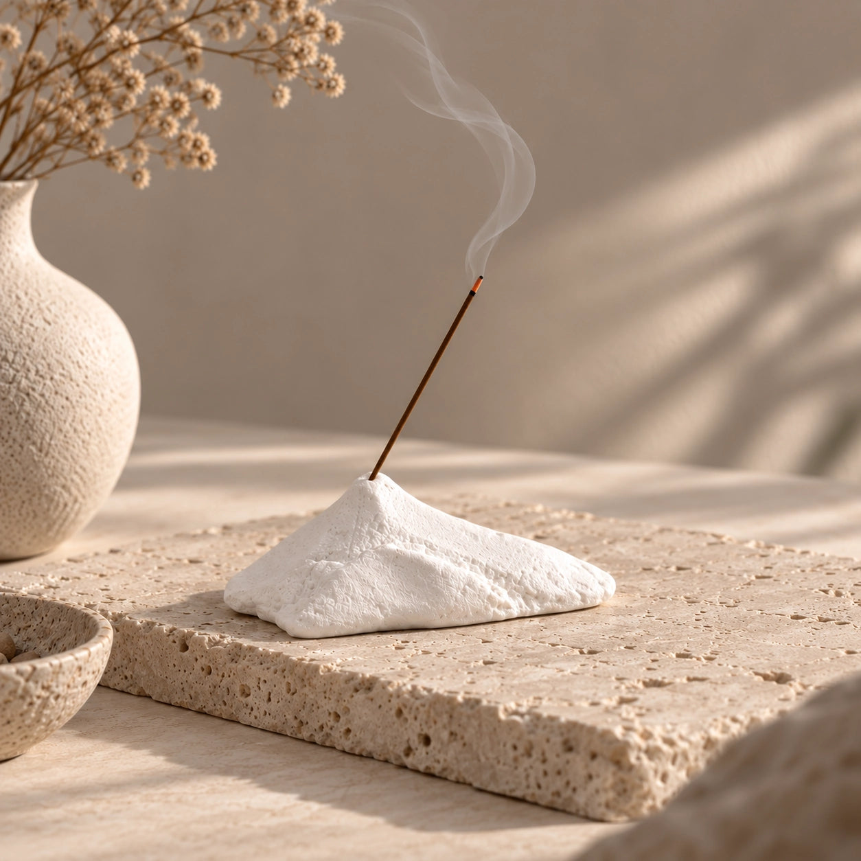 White sculptural mountain ceramic incense stick holder with smoke on a natural stone slab