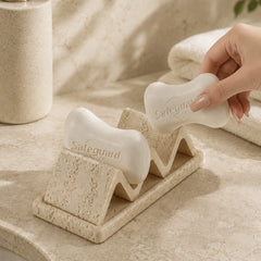 Natural sandstone soap dish holding soap bar with wave-shaped drainage slots